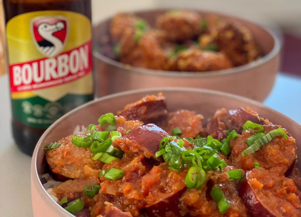 A bowl of caramelized meat dish garnished with green onions, served alongside a bottle of Bourbon beer