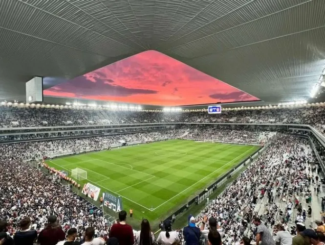 Panoramic view of a crowded football stadium during a France vs Turkey match in Bordeaux, with a spectacular red sunset visible above the stadium roof.