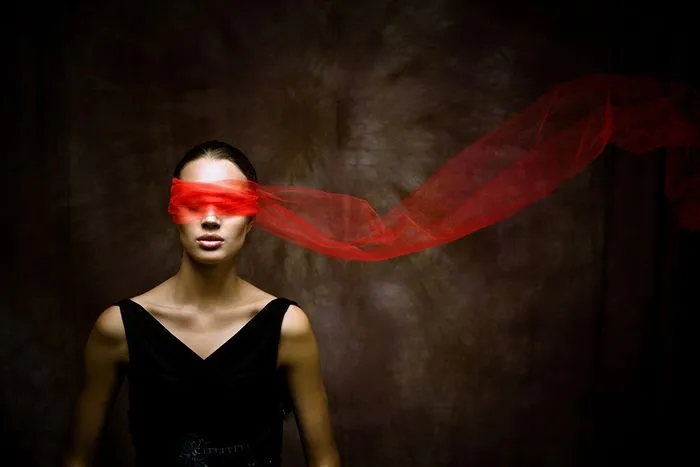 Woman blindfolded with flowing red fabric, wearing black dress against dark background, inspired by Bordeaux opera The Tsar's Bride