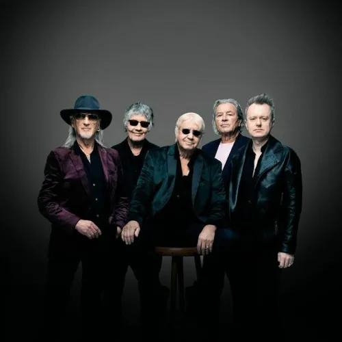 Group portrait of five Deep Purple musicians in black stage outfits and accessories, posed against a gray background.
