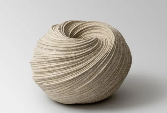 Spherical ceramic sculpture with undulating carved lines in light beige, displayed on a white background