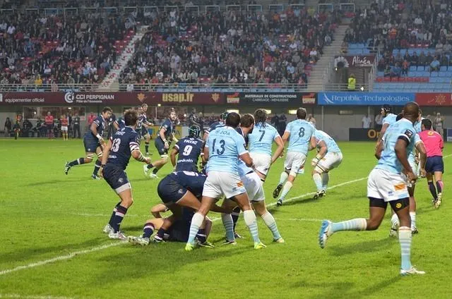 Top 14 rugby match featuring UBB players in light blue jerseys competing against dark-jerseyed opponents in a scrum at Bordeaux stadium