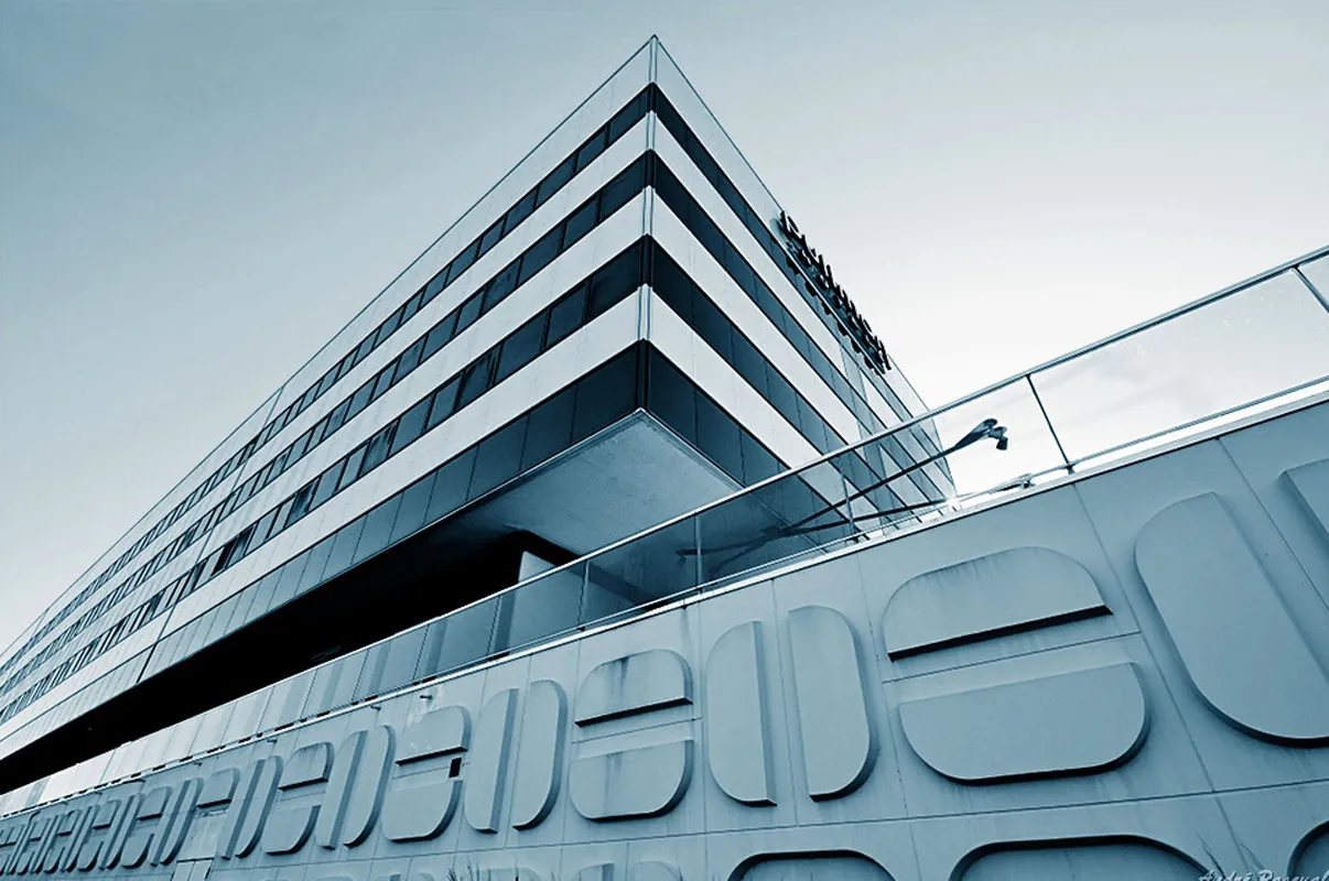 Modern facade of the Pullman Bordeaux Lac hotel featuring sleek glass and steel architecture with horizontal white and black bands, photographed from a low angle against a clear sky.