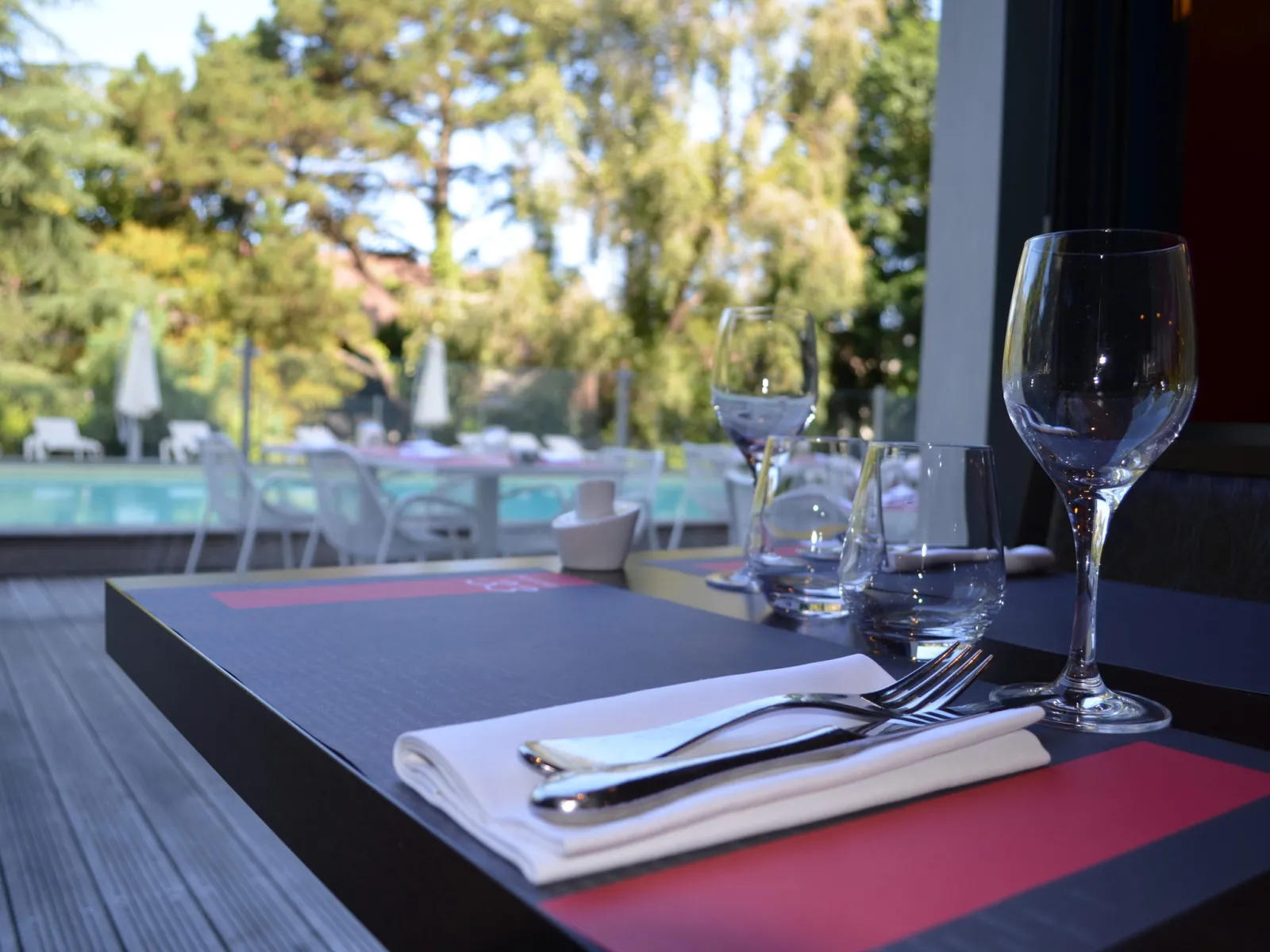 Restaurant table setting with water glasses, cutlery and white napkin, overlooking the lake and trees in the background at Bordeaux Lake