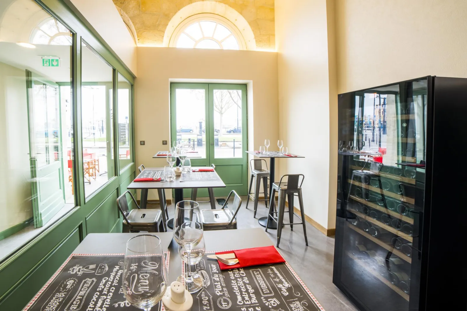 Modern restaurant dining room at Hôtel Vatel in Bordeaux featuring set tables, large green-framed windows overlooking the city, glassware and red napkins