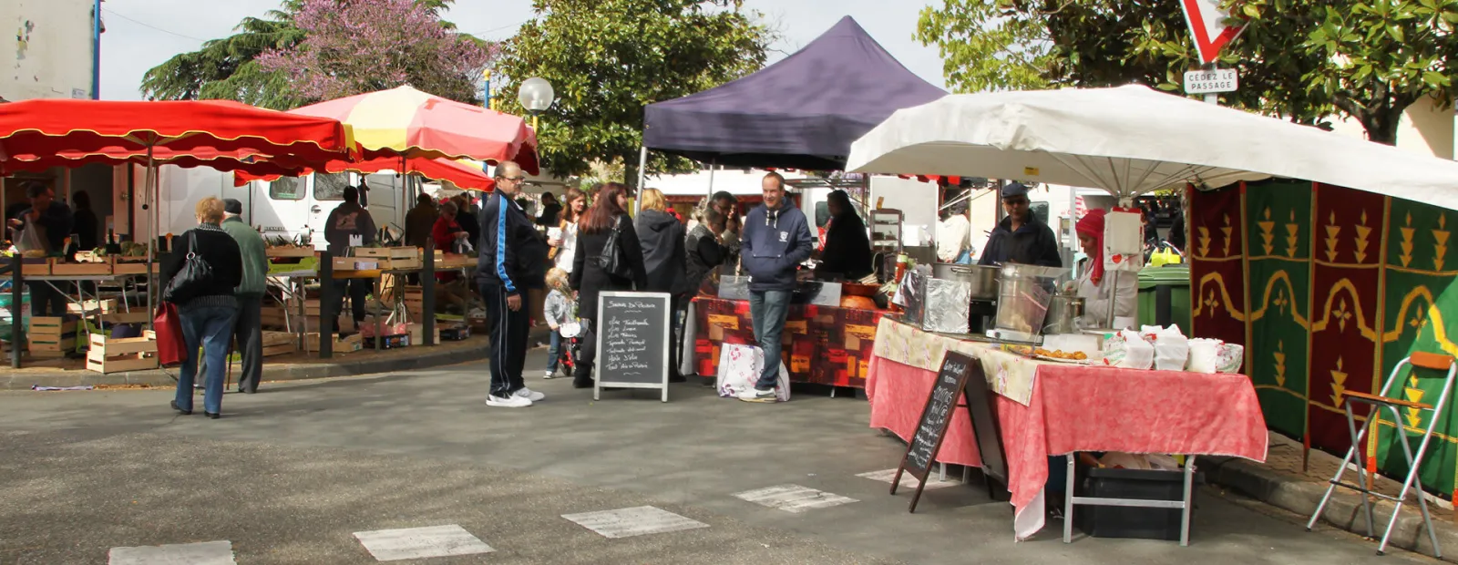 Overview of Bègles market in Bordeaux featuring colorful stalls under awnings and tents, with vendors and customers browsing fresh and artisanal products.