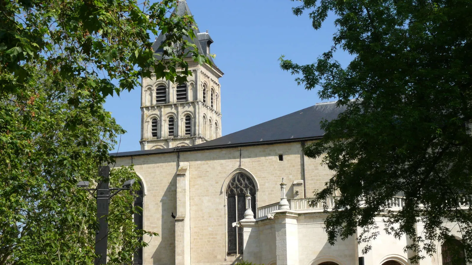 Basilica of Saint-Seurin in Bordeaux, a white stone church featuring a square bell tower with arcaded design, surrounded by green foliage.