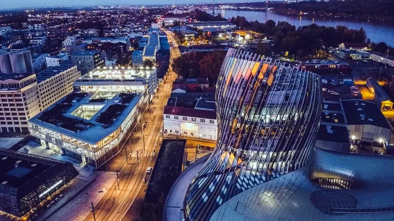 Nighttime aerial view of Bordeaux featuring illuminated modern architecture, the Garonne river, and the city skyline at dusk