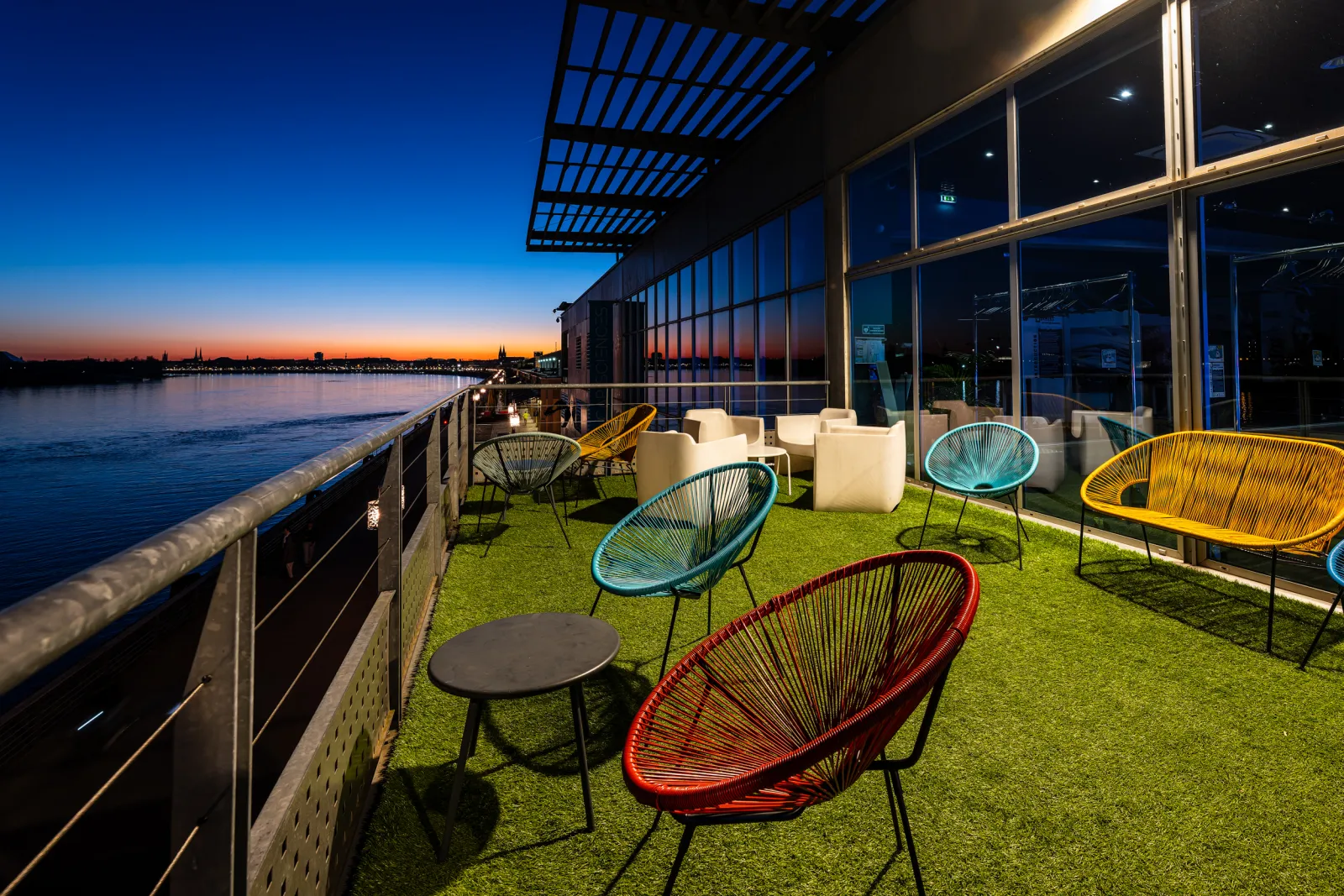 Cap Sciences rooftop terrace in Bordeaux at sunset featuring colorful modern chairs on artificial grass overlooking the Garonne river and lit cityscape