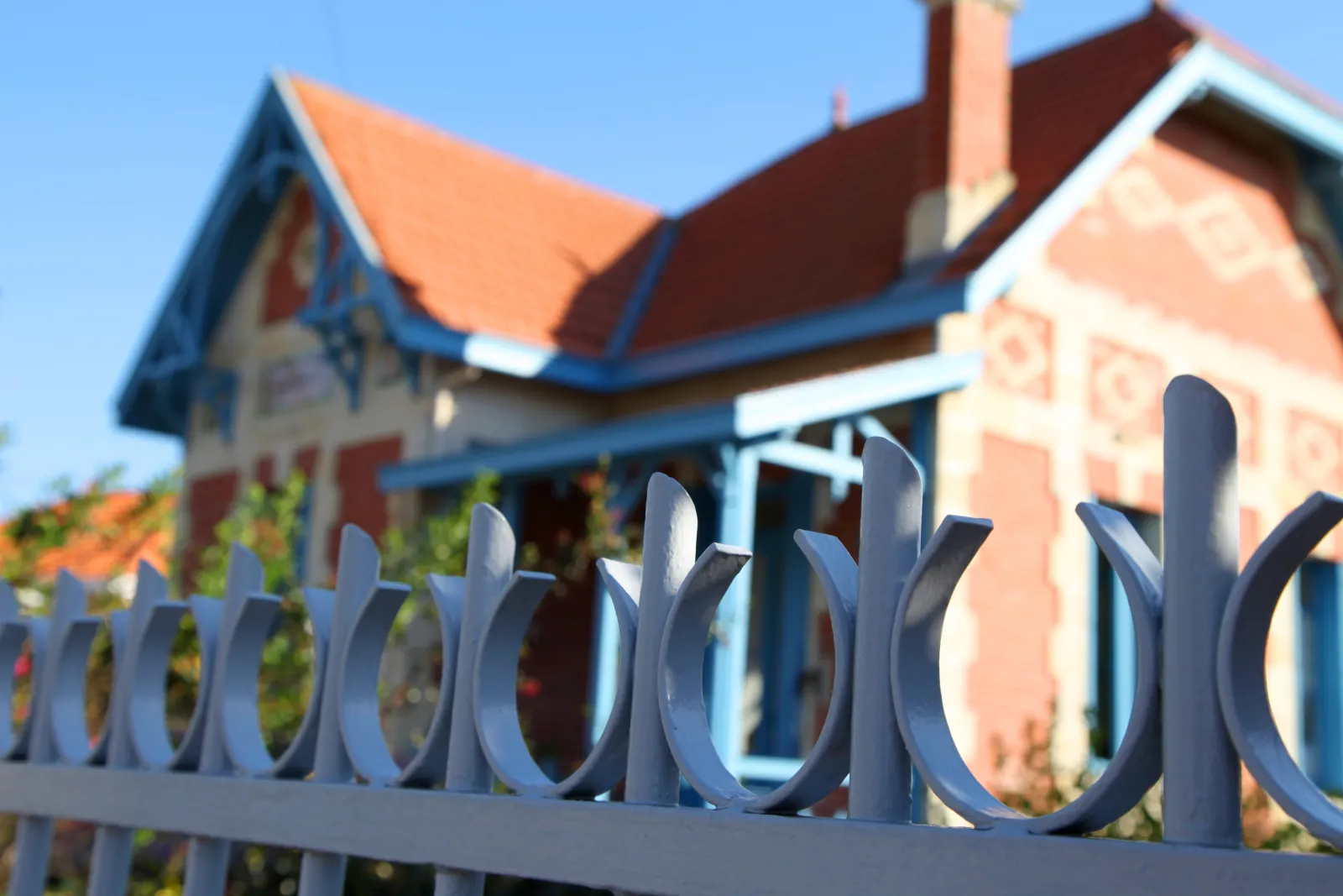 Blue wrought iron fence in front of a brick villa with red tile roof in Bordeaux