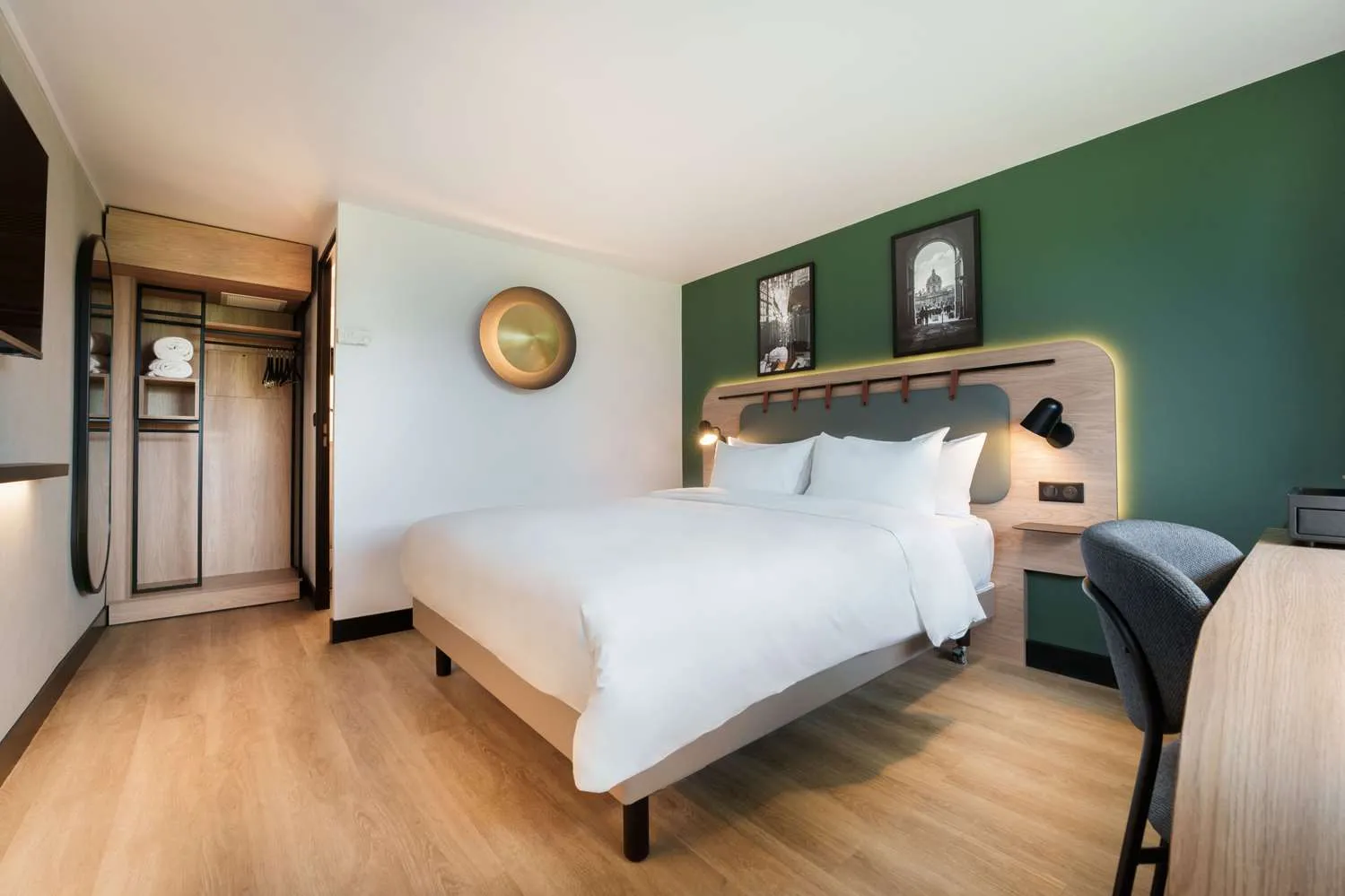 Modern hotel room at Campanile Nature Bordeaux Lac featuring a double bed with white linens, green accent wall, workspace, open wardrobe and contemporary bathroom