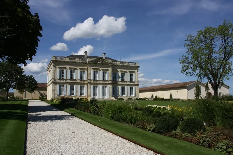 Front view of Château Gruaud Larose in Bordeaux, a classical-style mansion with two stories, regularly spaced windows, mansard roof, surrounded by manicured gardens and a gravel driveway.