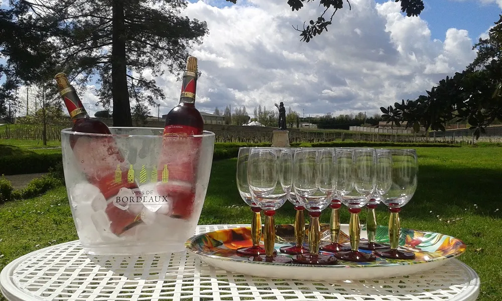 Outdoor wine service at Château Marquis de Vauban in Bordeaux featuring a champagne bucket with two bottles, six wine glasses, and views of the vineyards and countryside