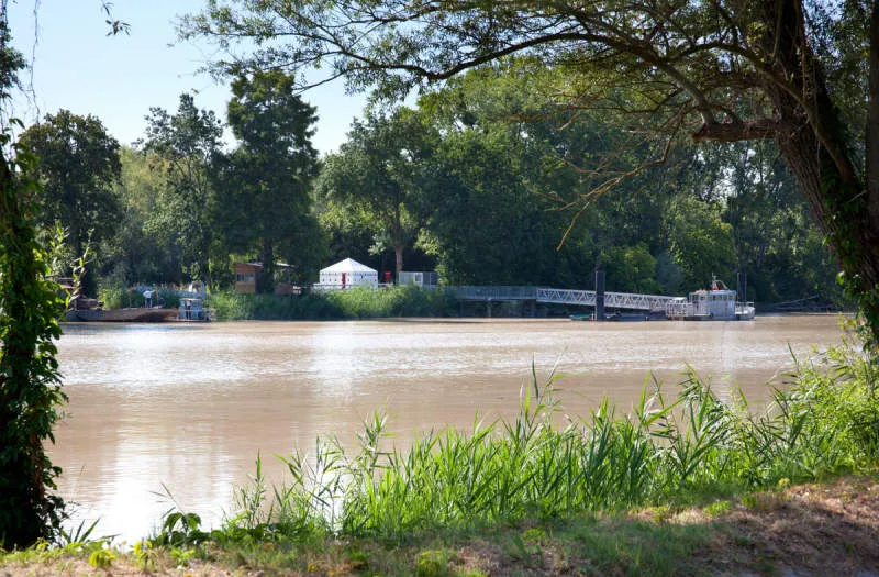 View of Île d'Arcins in Bordeaux with the swollen Garonne river, a white tent, and trees in the background