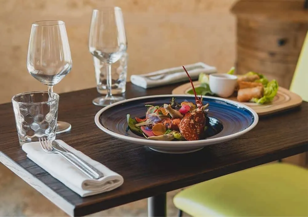 Elegant restaurant table setting with gourmet dish of meat and colorful vegetables, water glasses, white napkins and cutlery in a refined dining environment