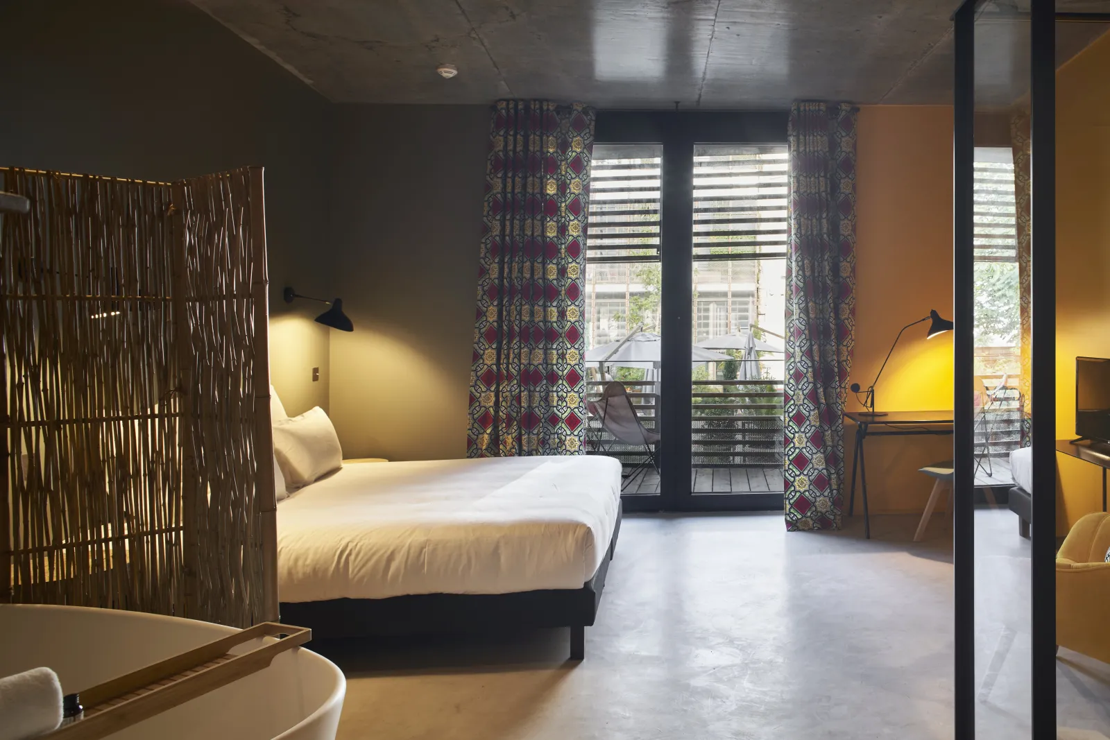 Modern bedroom at Hôtel La Zoologie in Bordeaux featuring a white bed, wooden partition, yellow walls, balcony access, and contemporary décor