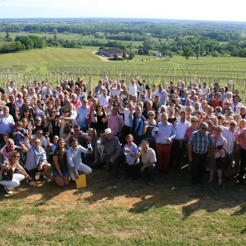 Large crowd of people gathered in the vineyards of Château Réaut near Bordeaux, with the château building visible on the hillside in the background