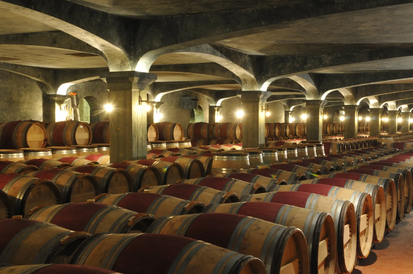 Underground wine cellar at Château Smith Haut Lafitte in Bordeaux featuring rows of oak barrels stored under lit concrete arches for wine aging.