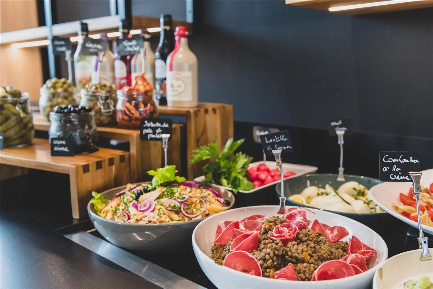 Gourmet buffet display featuring lentil salad, prepared dishes, wine bottles, and fresh vegetables in a restaurant dining room.