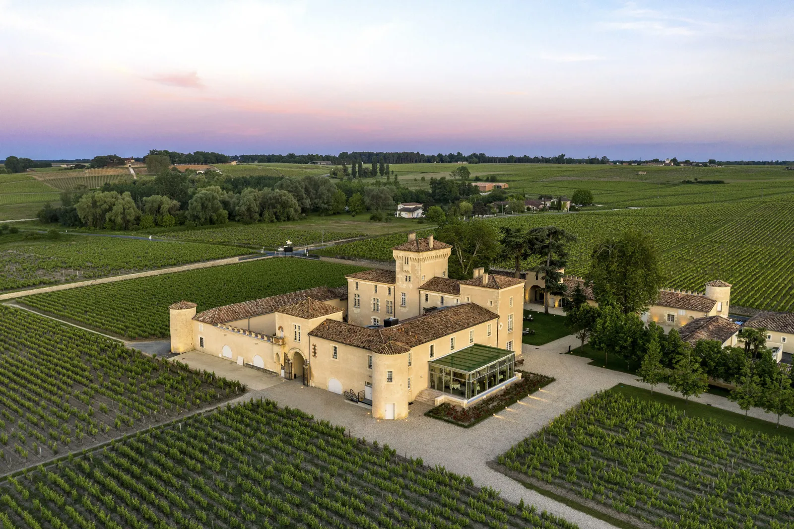 Aerial view of Château Lafaurie Peyraguey, a pale yellow-walled wine château surrounded by terraced vineyards in the Bordeaux region, at sunset.