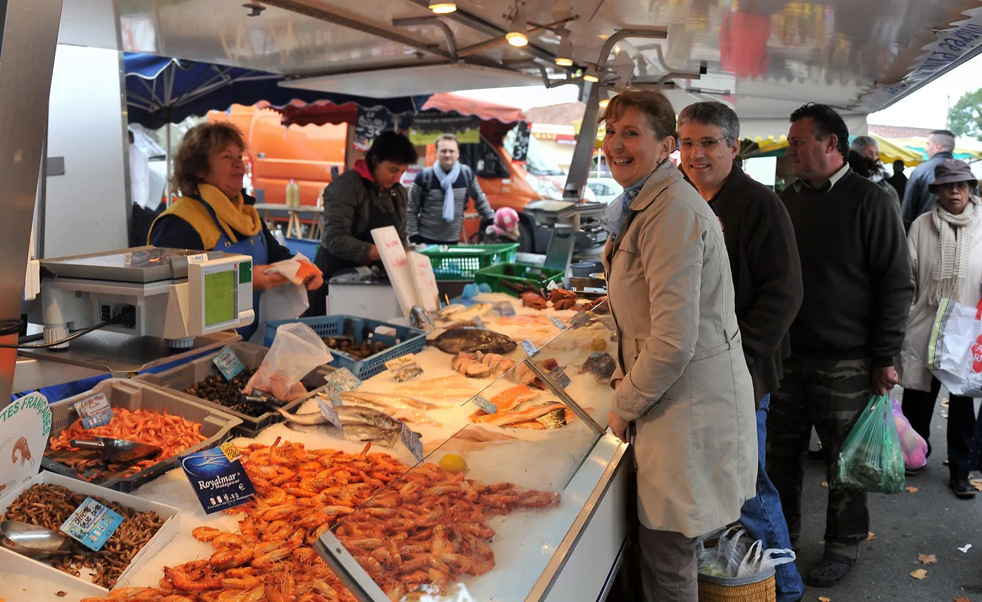 Fishmonger stall at Bassens market in Bordeaux displaying pink shrimp and fish, with smiling customers and sellers