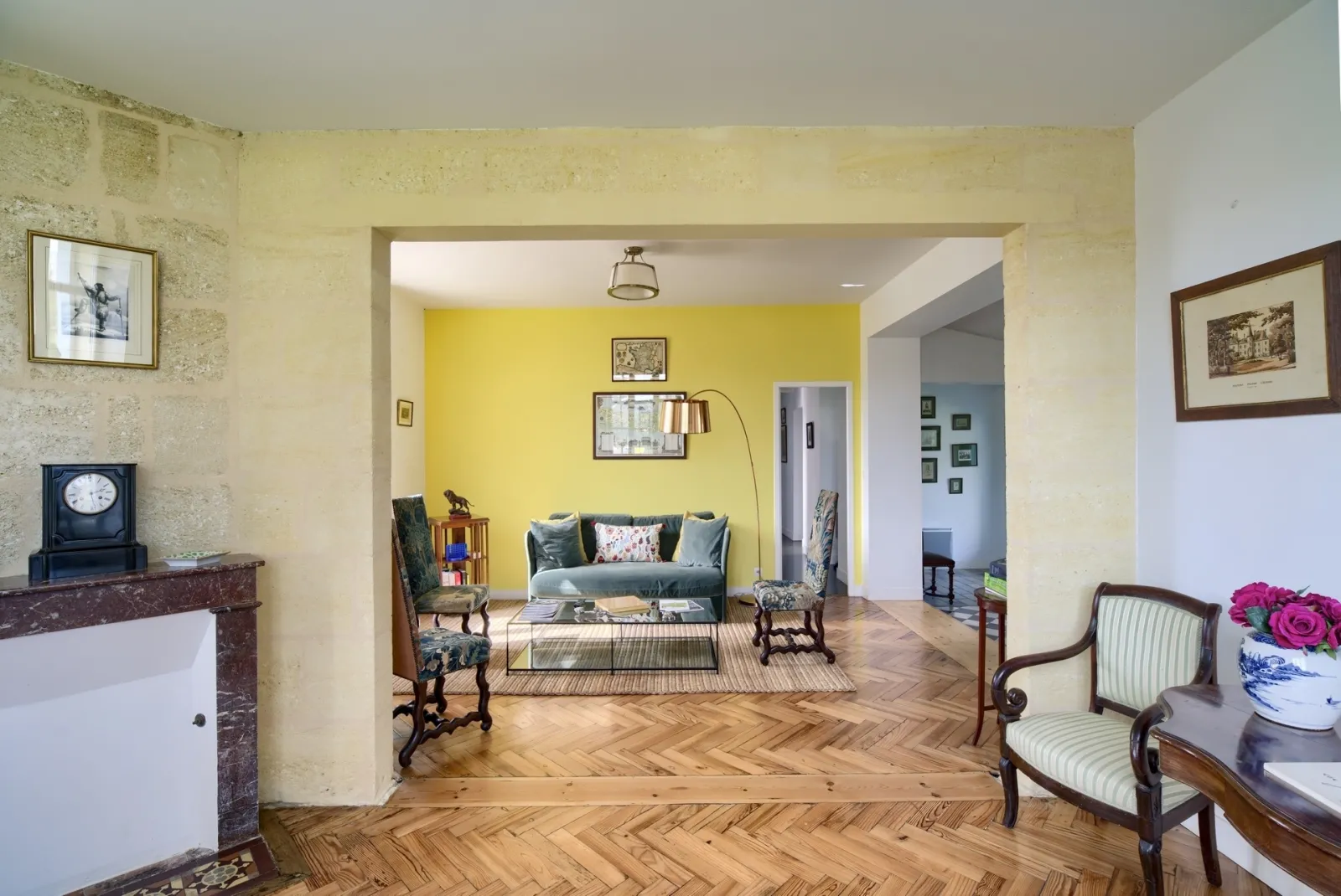 Spacious living room interior in Bordeaux featuring bright yellow walls, herringbone parquet flooring, classic wooden furniture, and openings to adjacent rooms