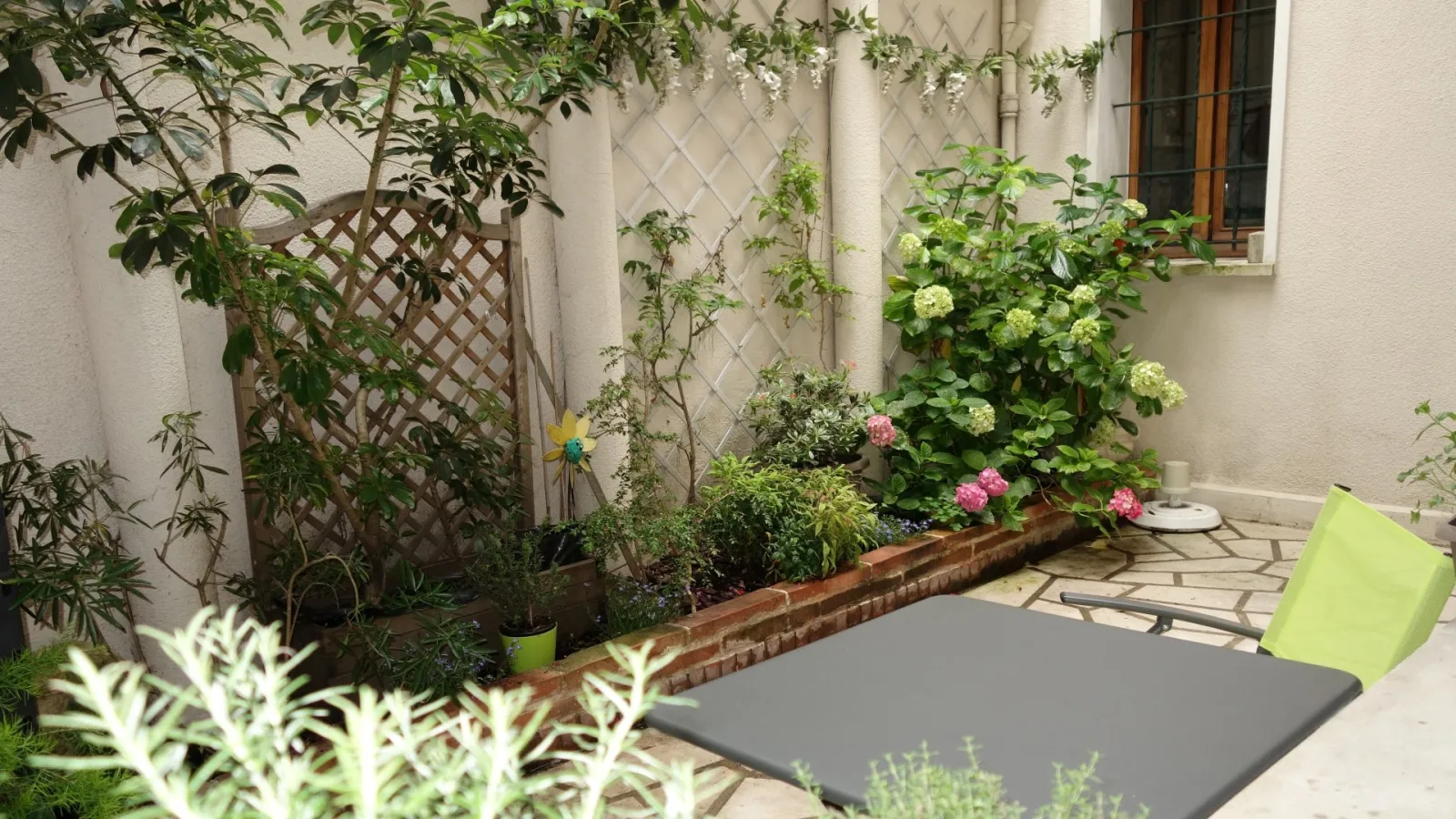 Small Bordeaux courtyard with paved terrace, garden furniture, potted plants and pink and white flowers along a brick wall.