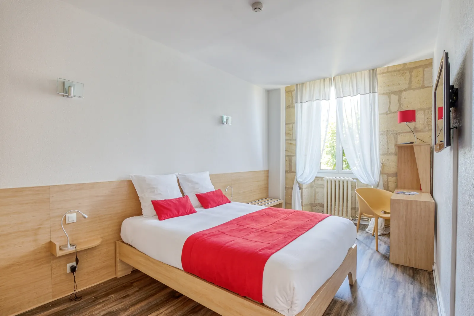 Modern hotel room with a light wooden double bed, white bedding and red blanket, at the Hotel des Voyageurs in Bordeaux
