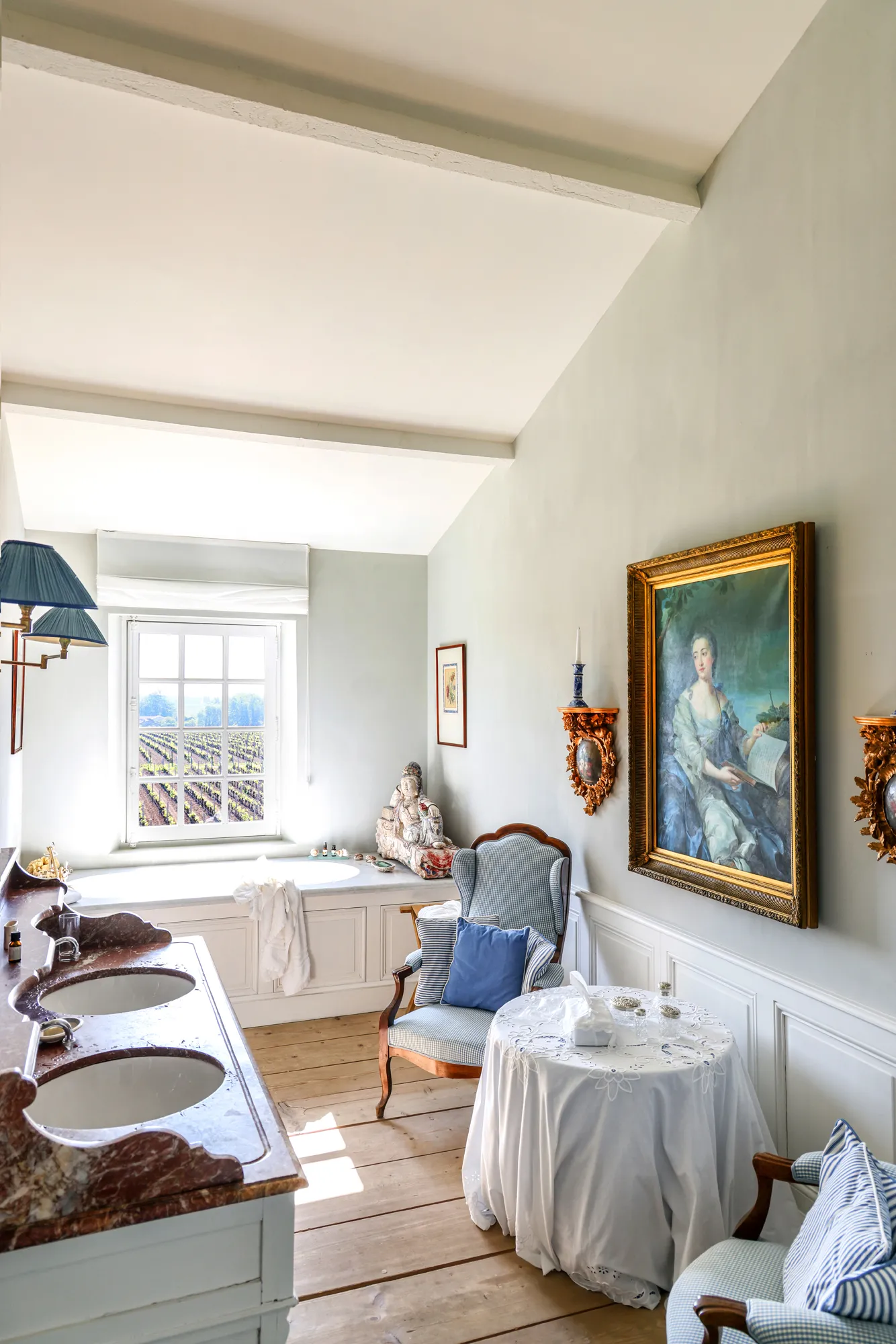 Elegant bathroom of a guest room featuring a bathtub by the window, framed portrait, 18th-century furniture and classic decor at Château du Tertre in Bordeaux.