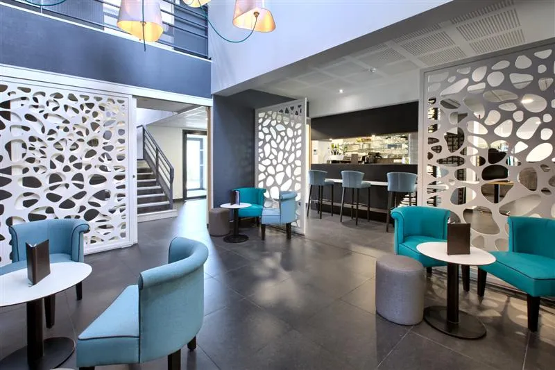 Modern lobby of Au Comté d'Ornon hotel in Bordeaux featuring turquoise armchairs, white perforated screens, bar area and contemporary furnishings