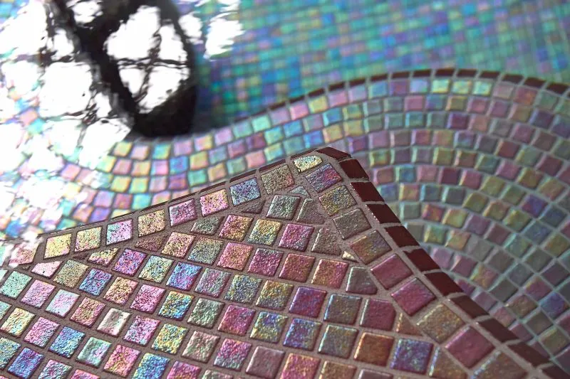 Close-up of iridescent colorful mosaic tiles in the swimming pool of the Calinésie aquatic center in Libourne, with natural light reflections and shadow detail.