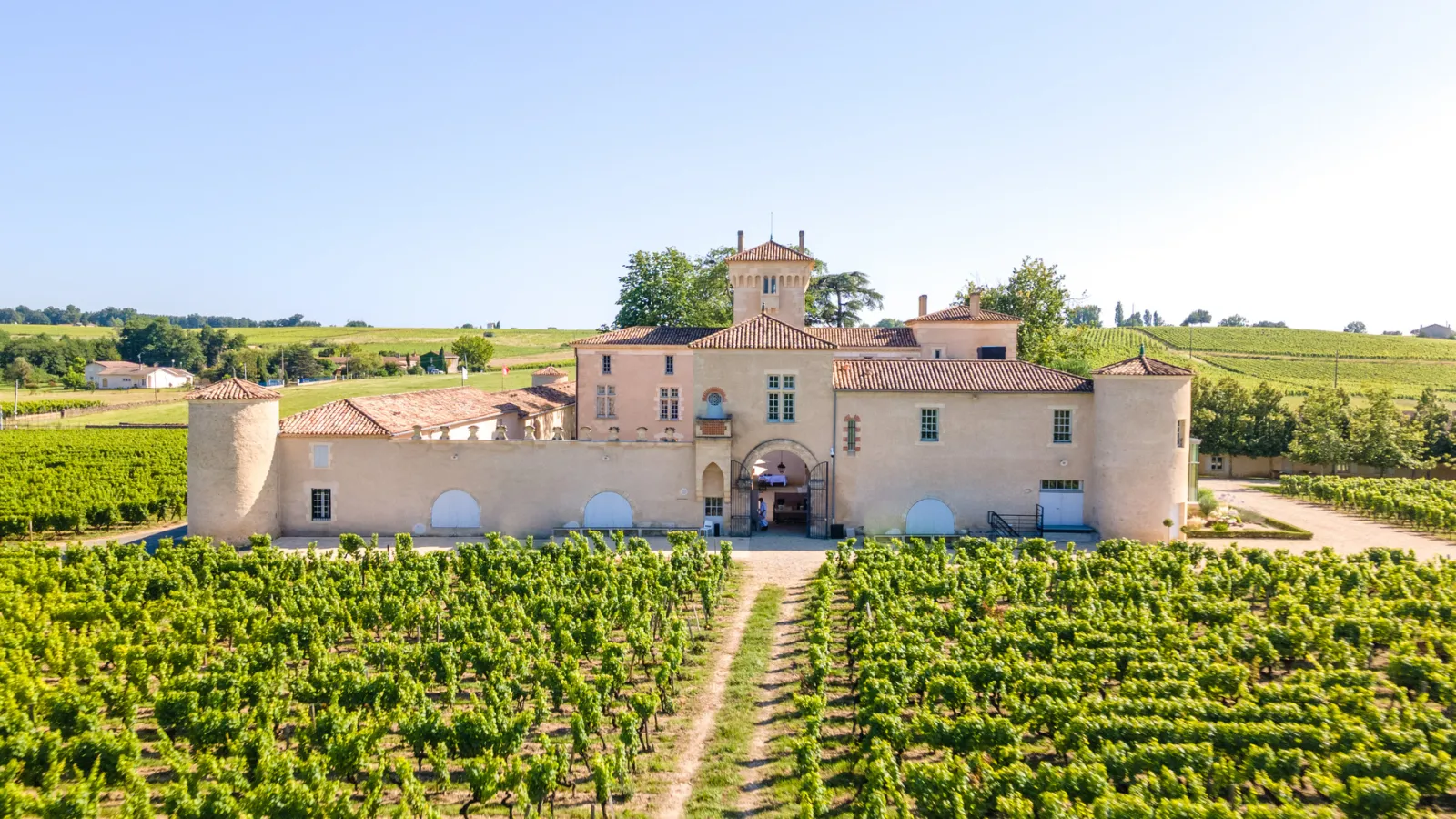Château Lafaurie-Peyraguey, a pink Aquitanian-style château surrounded by vineyards in the Bordeaux region, featuring distinctive towers and tiled roofs.