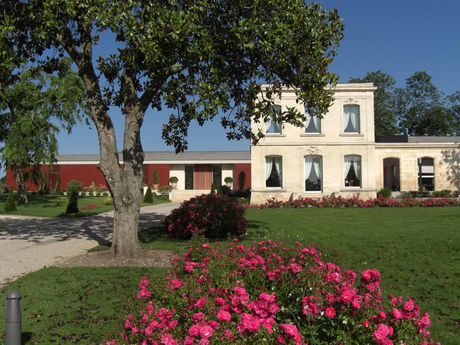 Luchey-Halde Castle in Bordeaux featuring white stone manor house, red building, manicured gardens with pink flowers and ancient tree
