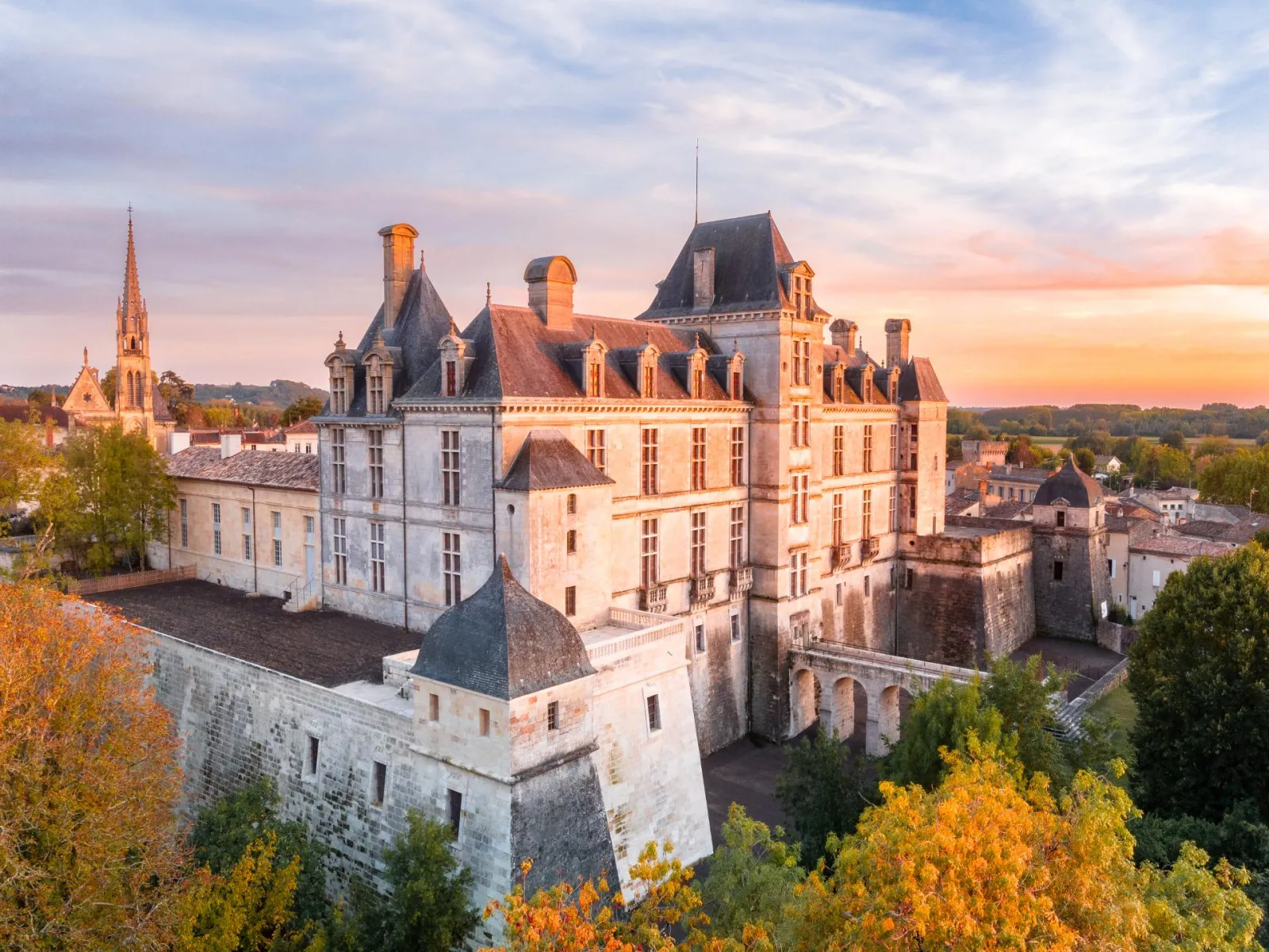 Aerial view of Cadillac Ducal Castle at sunset, a Renaissance fortress with slate roofs surrounded by fortifications, located near Bordeaux in Aquitaine.
