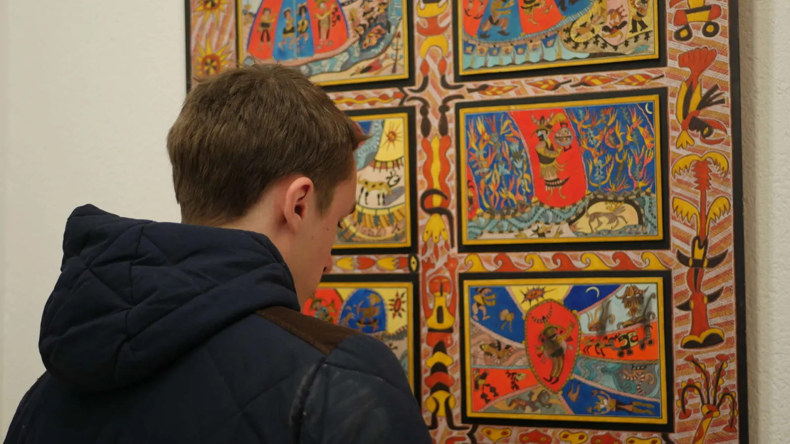 A child seen from behind wearing a black jacket gazes at a vibrant multi-panel artwork featuring geometric and figurative patterns in red, blue, yellow, and orange at the Musée de la Création Franche in Bordeaux.