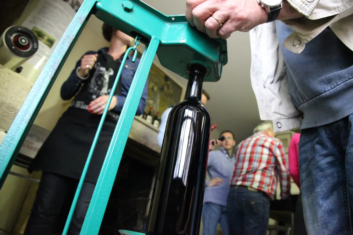 A black wine bottle hanging from a turquoise frame during a wine tasting in Bordeaux, with visitors in the background.