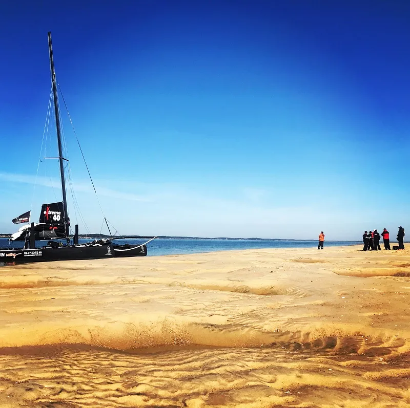 Black sailing yacht moored on a sandy beach with visitors in the background under clear blue sky