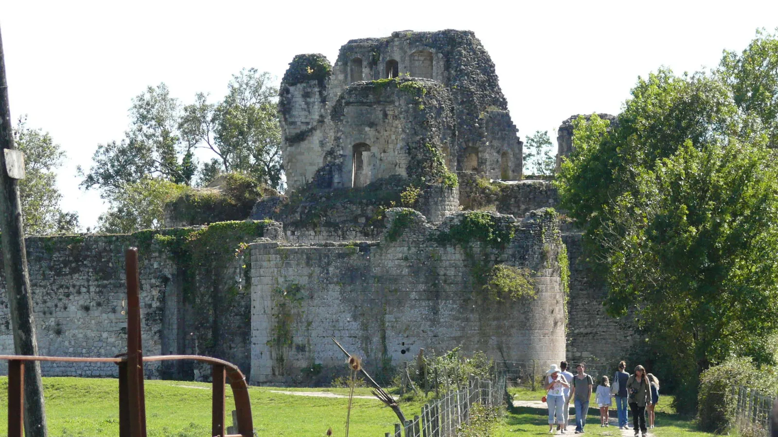 Ruins of the medieval Blanquefort fortress in Bordeaux, with its ivy-covered stone towers surrounded by greenery and visitors