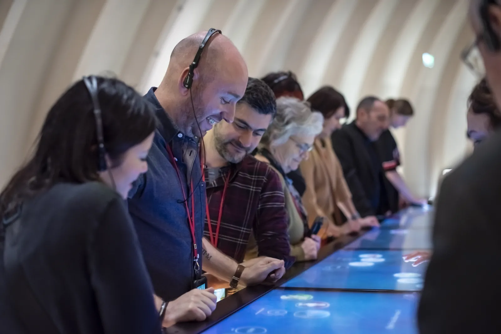 Group of visitors wearing interactive headphones exploring an interactive exhibition at the Cité du Vin in Bordeaux, with blue touchscreens displaying multimedia content.