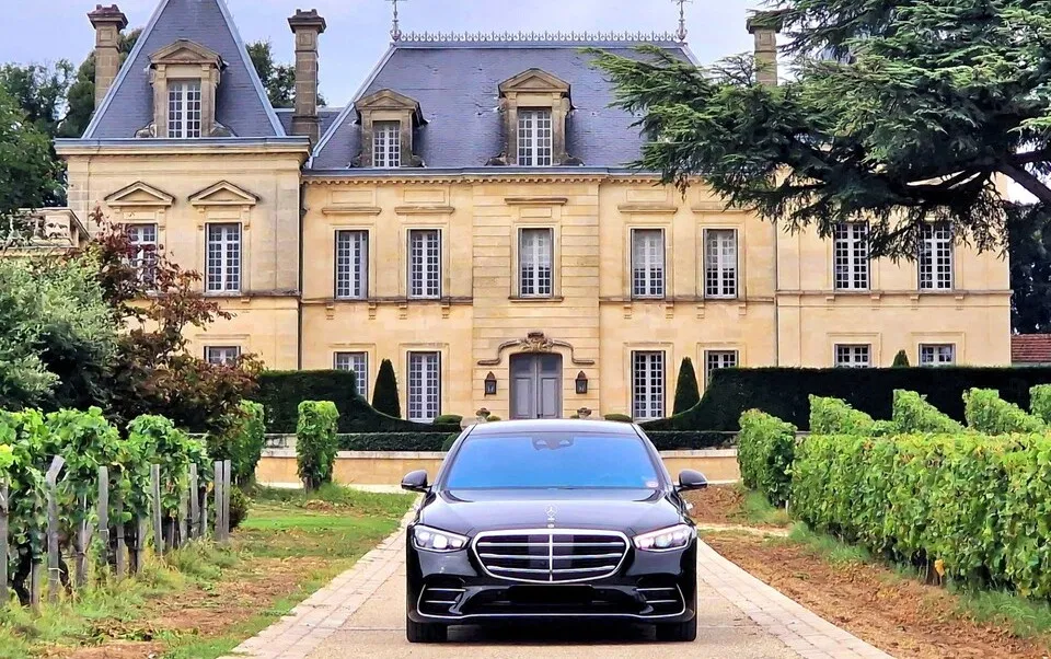 Black luxury car parked on a vineyard driveway in front of a Second Empire château with golden stone facades