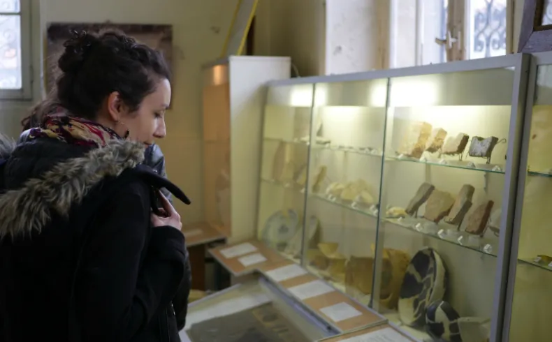 A woman views a museum display case with archaeological artifacts and ancient tools at the Musée des Amis du Vieux Lormont in Bordeaux.