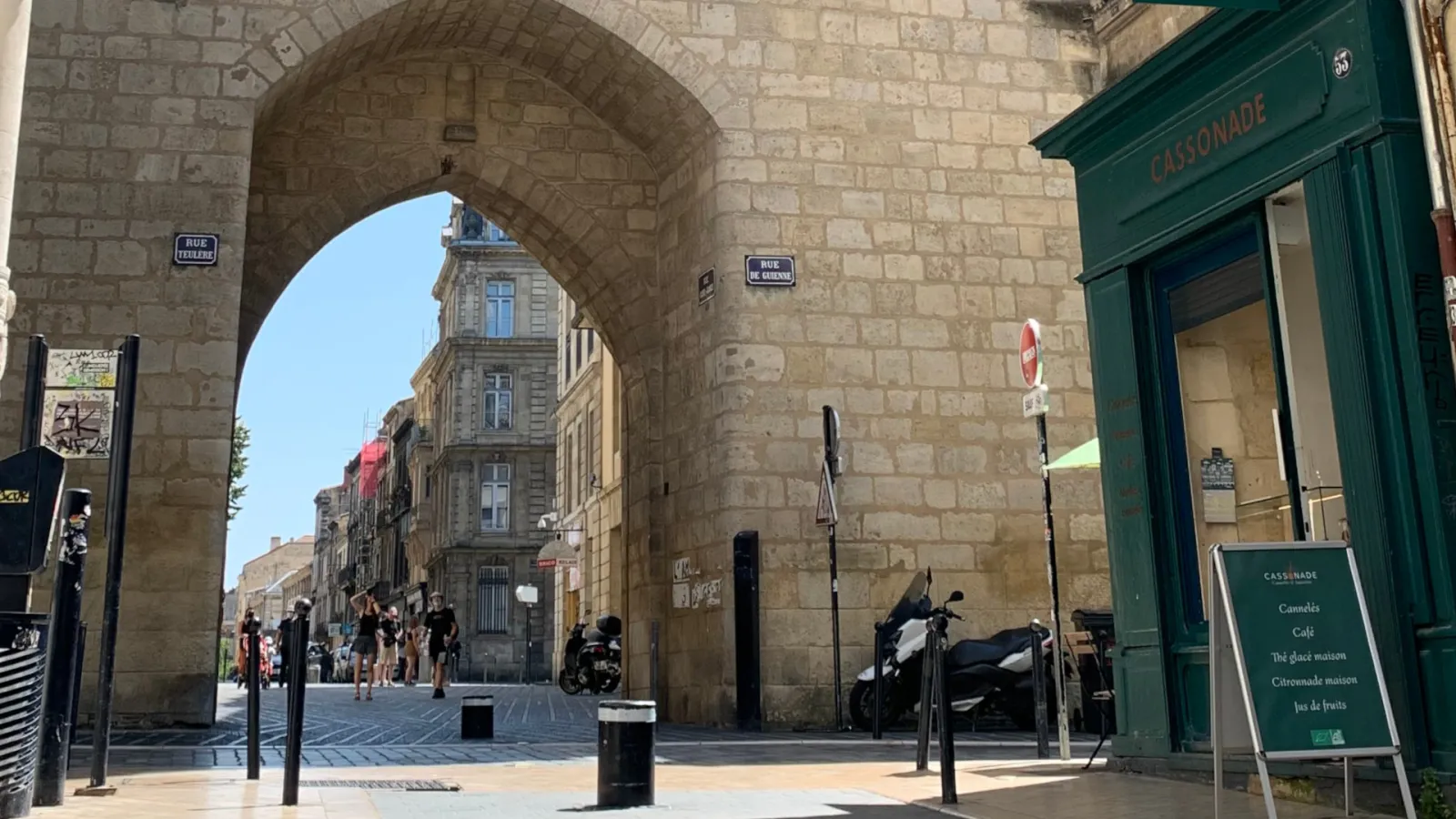 View of Rue de Cheverus in Bordeaux passing under a stone arch, with the Cassonade café visible on the right and Haussmann-style buildings in the background.