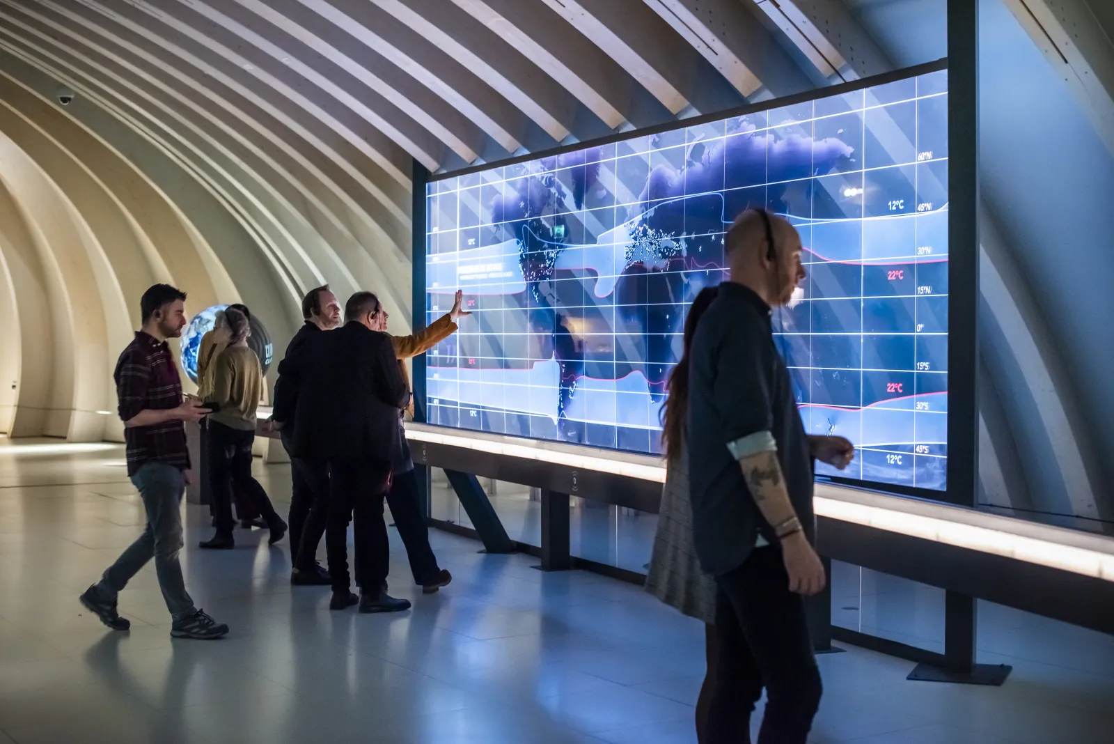 Visitors viewing a large interactive display screen showing a world map with climate data at the City of Wine in Bordeaux