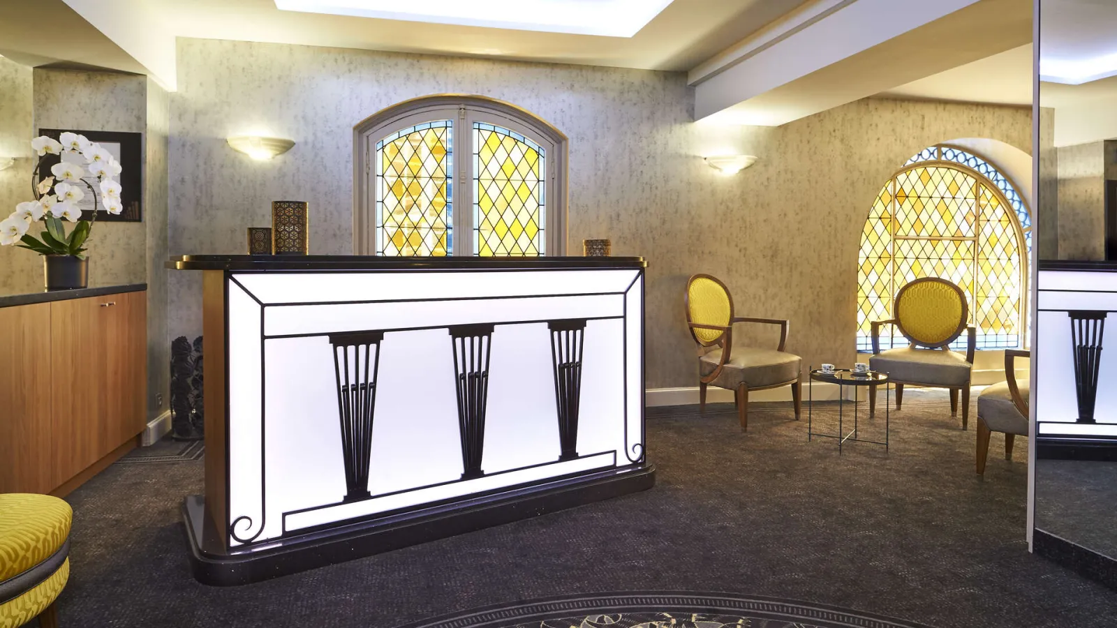 Elegant lobby of the Best Western Premier Hôtel Bayonne Etche Ona in Bordeaux, featuring an illuminated reception desk, yellow armchairs, diamond-patterned windows and art deco style