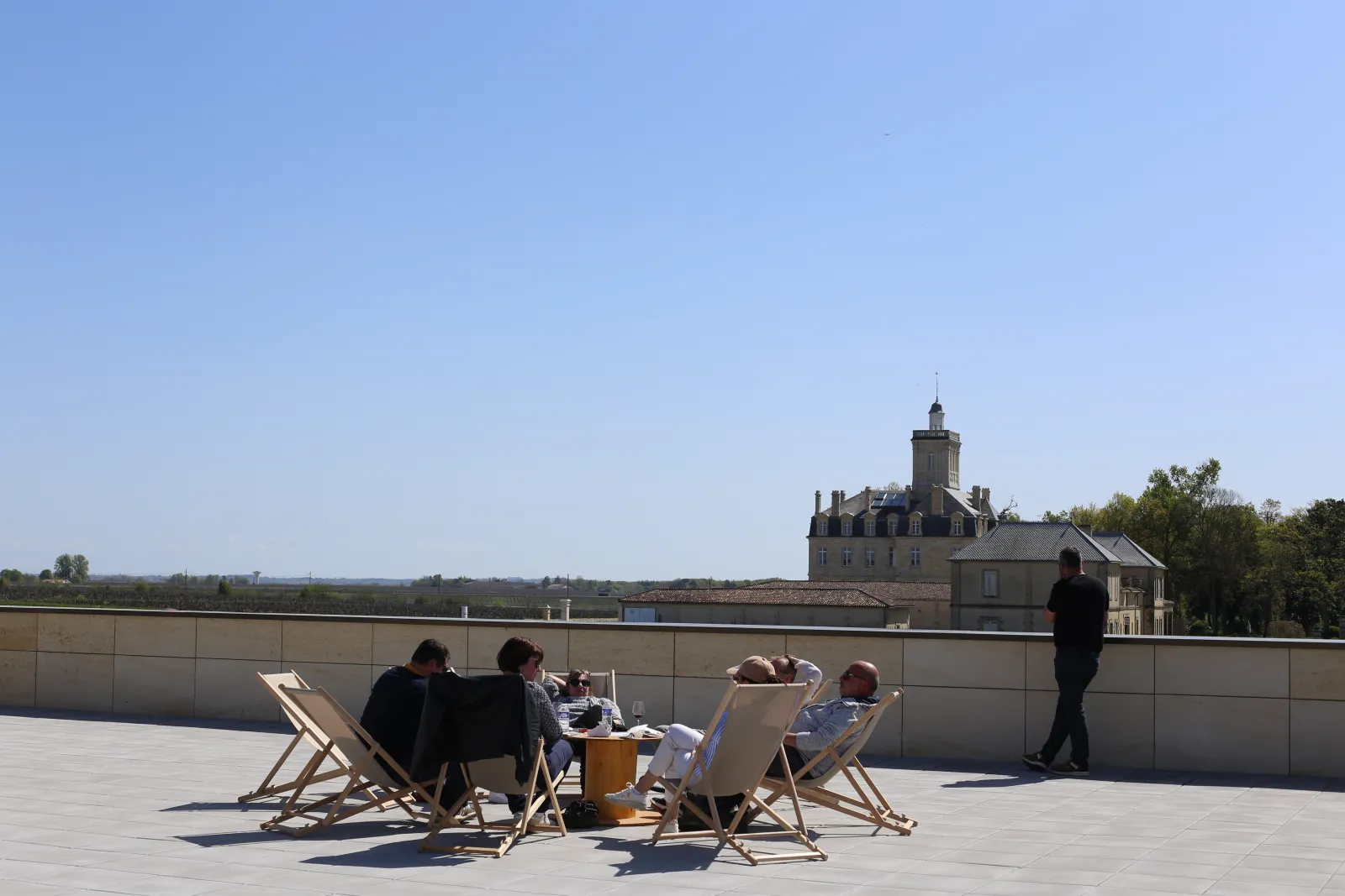 A group of people relaxing in deck chairs on a terrace overlooking Château Larose-Trintaudon in Bordeaux.