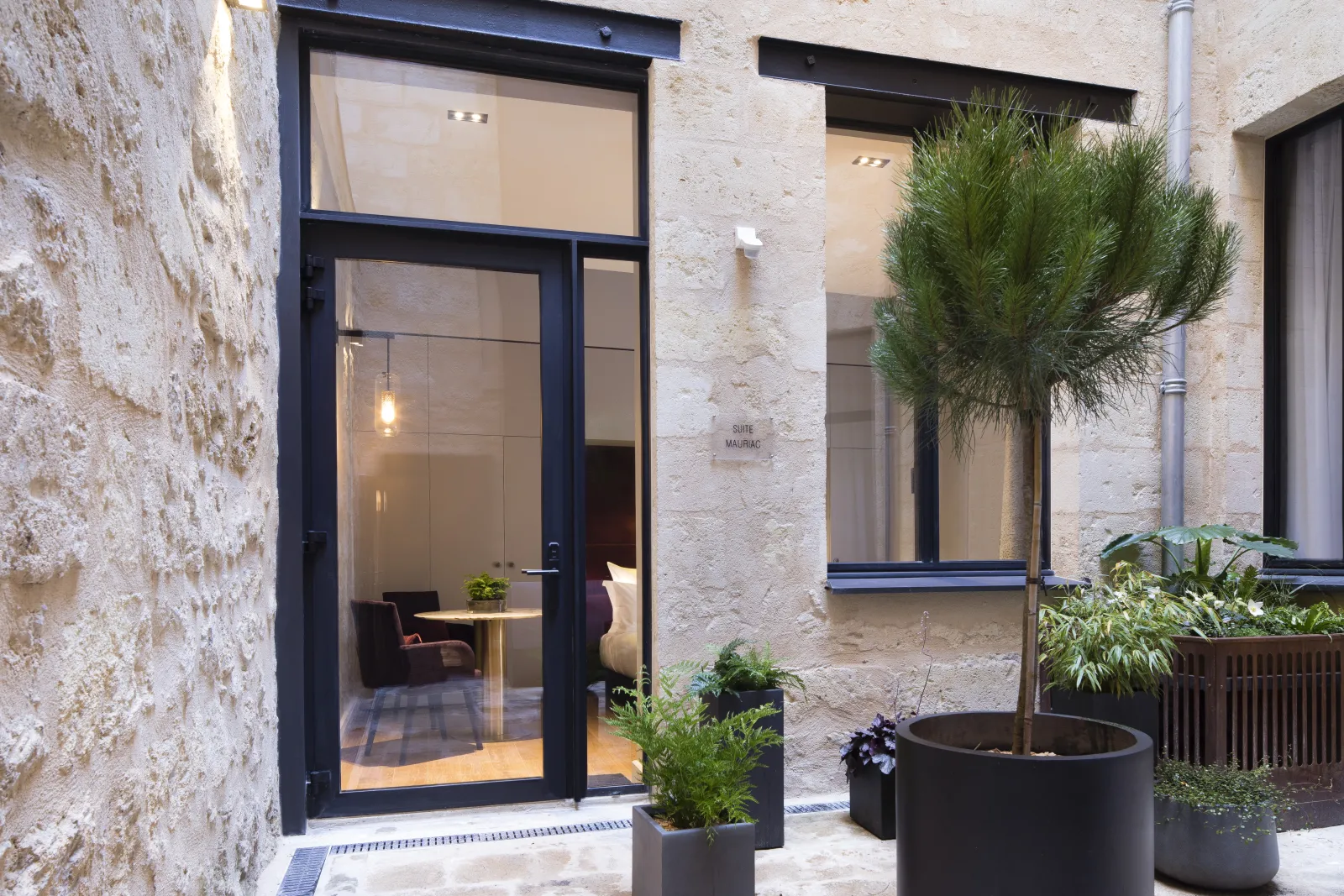 Entrance to Hotel Cardinal Bordeaux featuring black glass door, beige stone façade, paved courtyard and potted plants