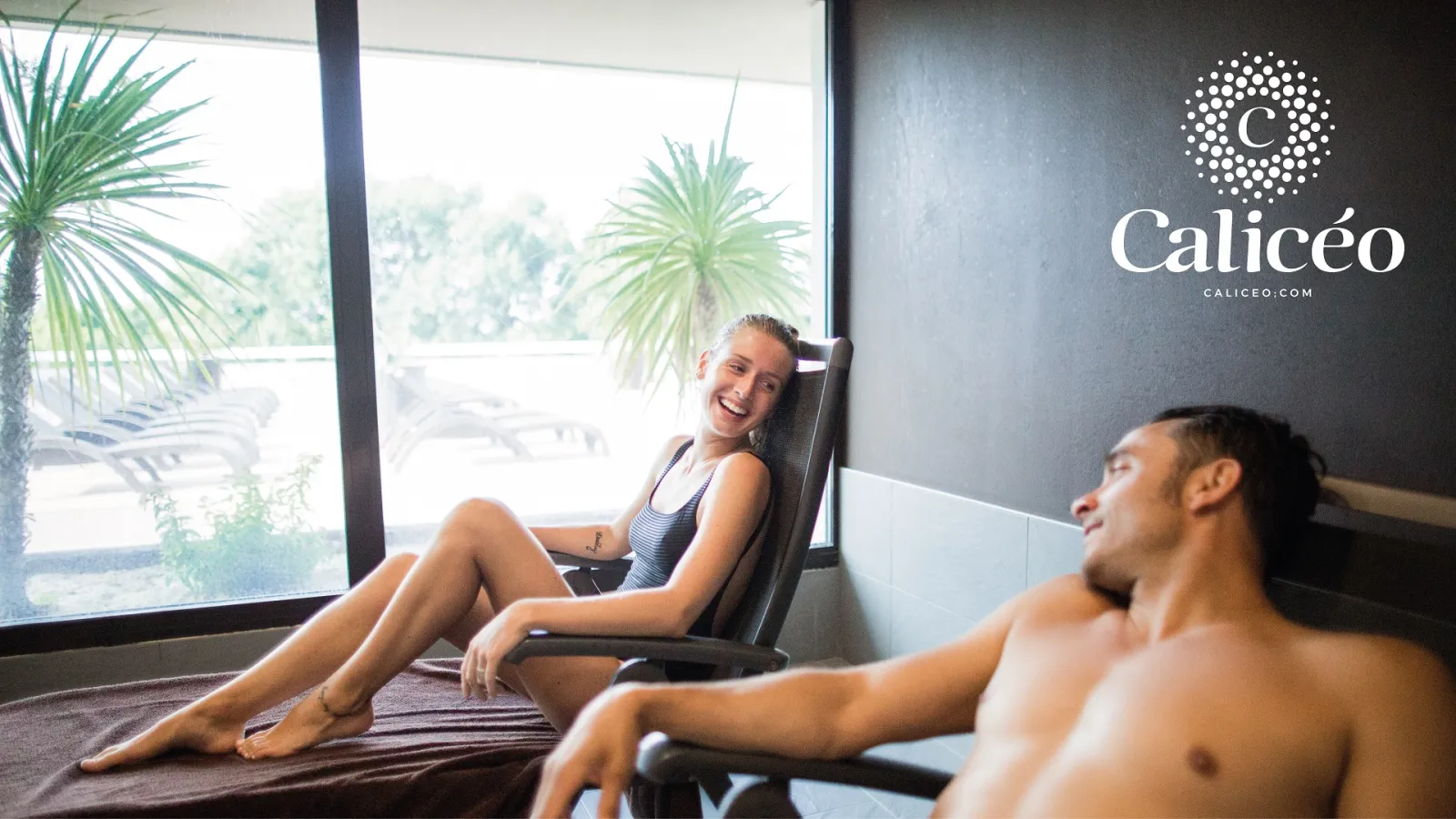Two relaxed people in a modern wellness space overlooking Bordeaux, with palm trees and panoramic windows, Calicéo logo displayed