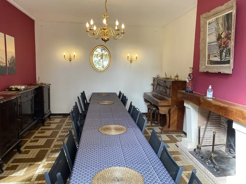 Elegant dining room at Château La Gontrie in Bordeaux featuring a long blue table, black chairs, red and white walls, brass chandeliers, fireplace and classical decor