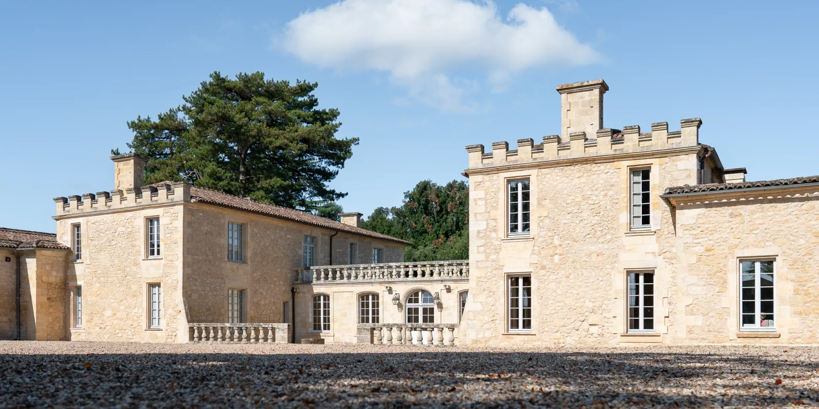 Facade of Château de Ferrand near Bordeaux, stone manor house with crenellated towers, balustrades, and mullioned windows surrounded by greenery.