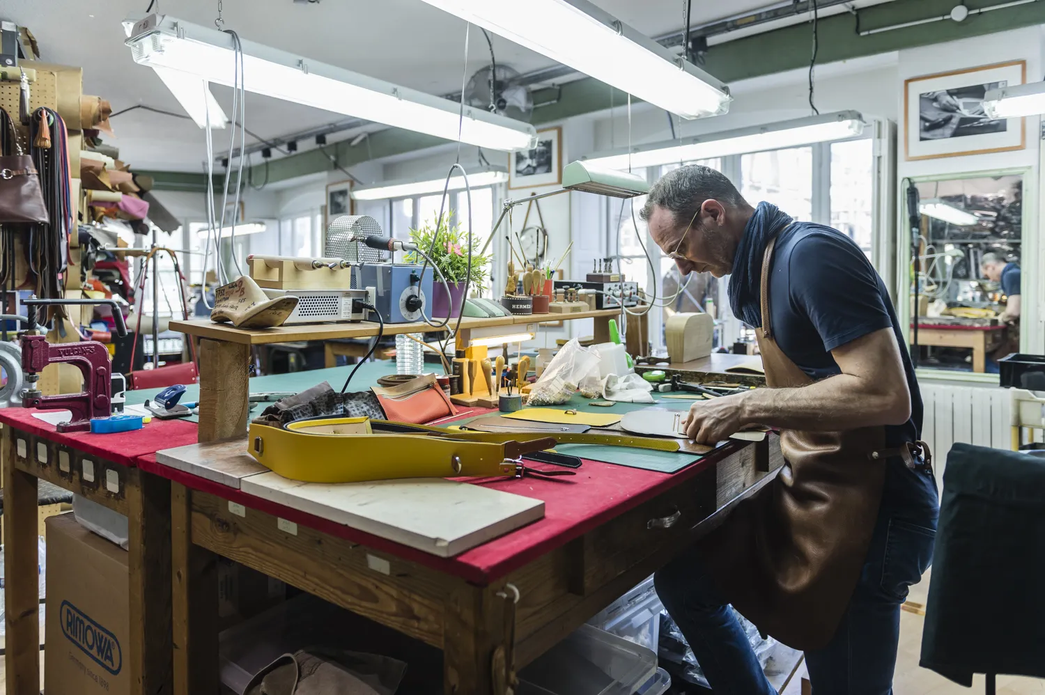 Craftsman working with leather at a workbench in a Bordeaux workshop, surrounded by colorful materials and tools